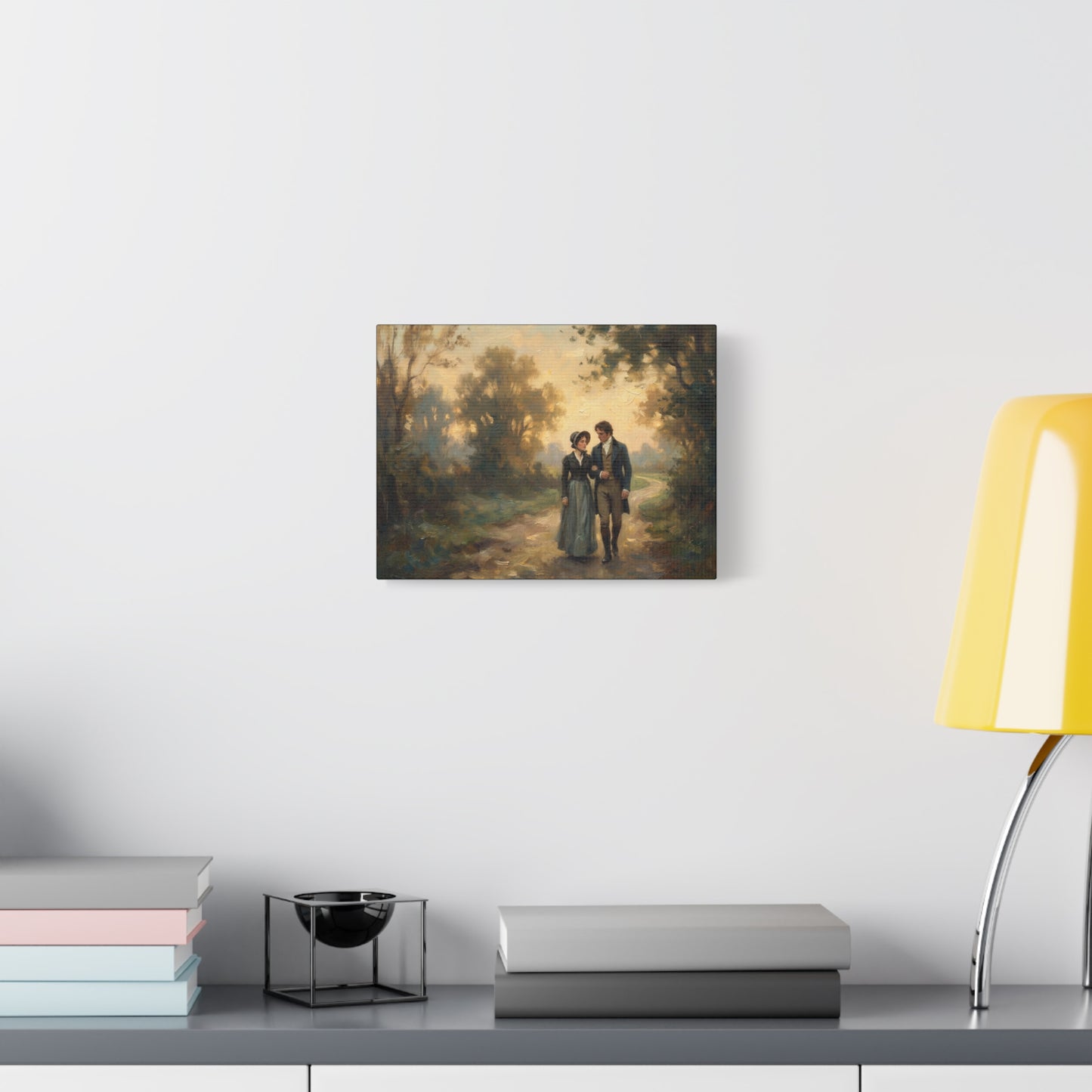Framed painting of a couple walking in a forest on a wall above a desk with books and a lamp.